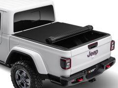 A white Jeep Gladiator's rear view shows a partially opened black tonneau cover over the bed, featuring the Jeep logo on the tailgate and rugged off-road tires.
