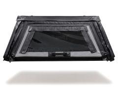 Front view of a FLATED® inflatable truck topper rear window assembly with a smoked transparent vinyl window, reinforced black PVC outer frame, zippered side panels, hook-and-loop weather flaps, integrated carry handle, and D-ring tie-down points, shown fl