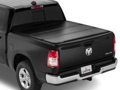 Black pickup truck with a hard tonneau cover, displaying a shiny RAM logo on the tailgate.