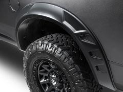 Close-up of an off-road vehicle's wheel and fender, showcasing a rugged, deeply treaded tire and a textured matte black fender trim with angular design.