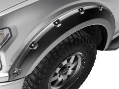 Close-up of a silver vehicle's fender with a matte black fender flare and rugged tire, featuring metallic fasteners and a multi-spoke wheel.