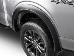 Close-up of a silver pickup truck's wheel area featuring a black fender flare and alloy wheel with a rugged tire.