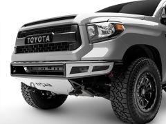 Close-up of a gray Toyota Tundra pickup truck's front end, featuring a black grille with "TOYOTA" and chrome bumper details.