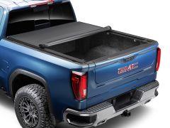 Rear view of a blue GMC pickup truck with a rolled-back black tonneau cover, showcasing its emblem, tail lights, and rugged tires.