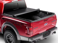 Rear view of a red Ford Raptor pickup truck with a rolled-up black bed cover, showcasing rugged tires and a distinct "RAPTOR" logo.