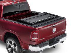 Red pickup truck rear view with a black retractable bed cover partially rolled up, showcasing smooth cargo bed and RAM logo on tailgate.