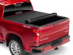 Red Chevrolet Silverado truck with a partially rolled-up black tonneau cover and visible rear badges.