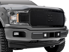 A close-up view of a grey pickup truck's front end, featuring a large black mesh grille with "X METAL," angular headlights, and rugged off-road tires.