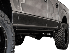 Close-up view of the lower section of a metallic gray pickup truck, showcasing large, rugged black tires and a textured dark trim along the bottom on a white background.