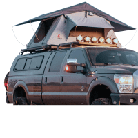 A modified gray Ford pickup truck with off-road tires and a rooftop tent in a grassy field, illuminated by spotlights.