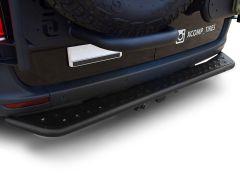 The image shows the rear end of a vehicle, specifically focusing on the bumper area. The bumper is black, featuring a robust and slightly textured surface with small circular indentations for grip. A spare tire is mounted just above the bumper, partially 