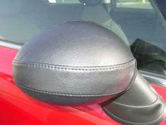 Black leather car mirror cover on red vehicle.