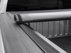 A close-up of a rolled-up black truck bed cover on a gray truck bed, partially unrolled and secured with velcro.