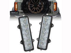 Two LED light bars in black casings, positioned in the foreground, with a Ford vehicle and its illuminated rear lights visible in the background.