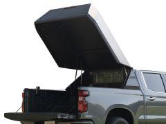 Gray pickup truck with the tailgate down and a raised, angular truck bed topper lid, showing the open cargo area and interior paneling against a clean white background.