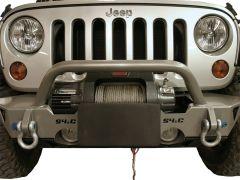 Close-up of the front of a silver Jeep, featuring a robust off-road bumper with a winch and hooks. A black license plate holder is angled downwards.