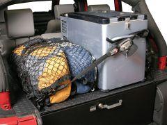 Cargo area of a vehicle with a portable fridge and bags secured with a net and straps. Interior has a practical and organized setup.